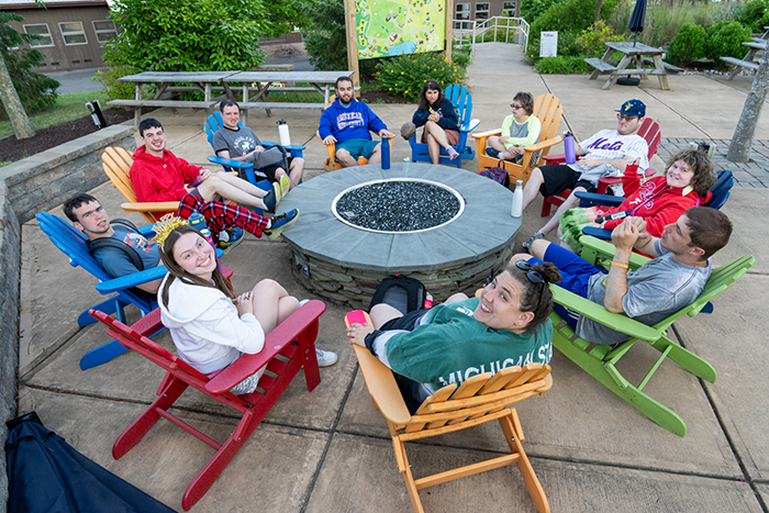 Photo of a group of young adults sitting around a fire pit at Camp Harlem