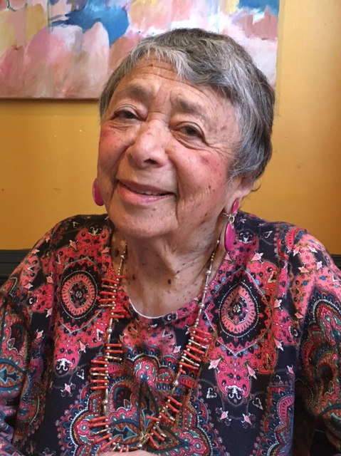 Photo of an elderly and smiling Agi Rado with short grey hair and wearing a pink patterned blouse
