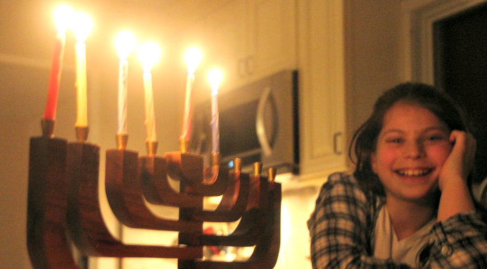 Smiling girl looking on at a partially lit menorah