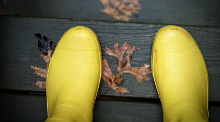 Yellow raise boots on a wet wooden surface covered in leaves 