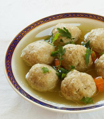 White bowl with blue edge containing soup crowded with matzah balls