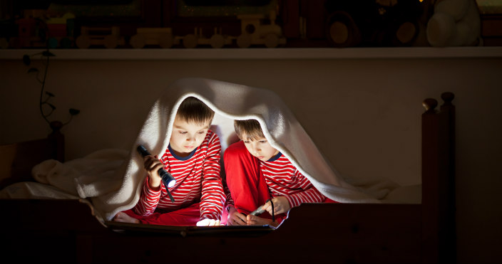 Two little boys with flashlights reading in a blankey fort