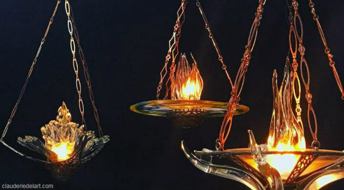 Three ner tamid eternal flames made of glass and hanging against a black background 