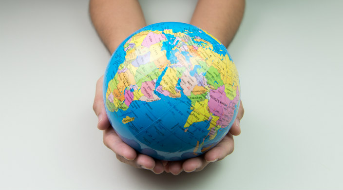 Hands holding a small and fragile globe against a white background 