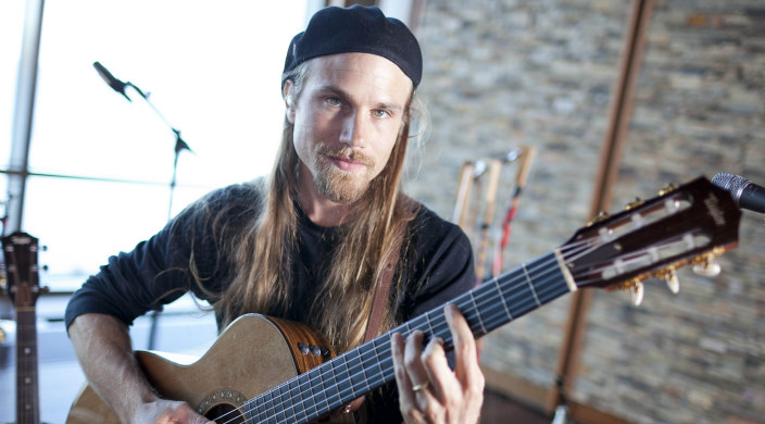 Headshot of musician Guy Mendilow with long blond hair and a hat holding a guitar