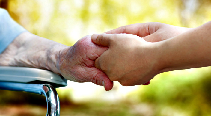 Hand of an elderly person held by the hand of a younger person