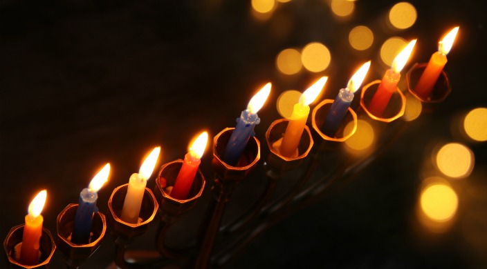 Hanukkah menorah with all the candles lit, and other lights in the background