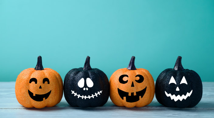 Four glittery black and orange jackolanterns against a teal backdrop 