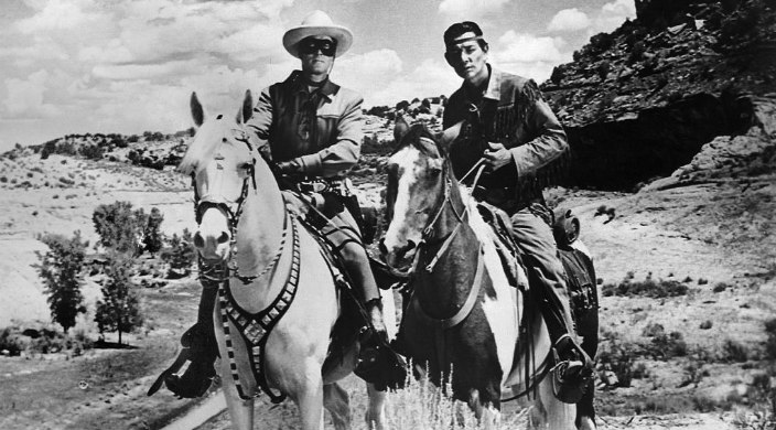 Black and white photo of the Lone Ranger and Tonto each on horseback with a western landscape in the background