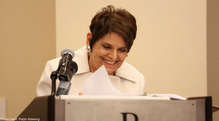 A shorthaired Rabbi Lynne Landsberg speaking at a podium