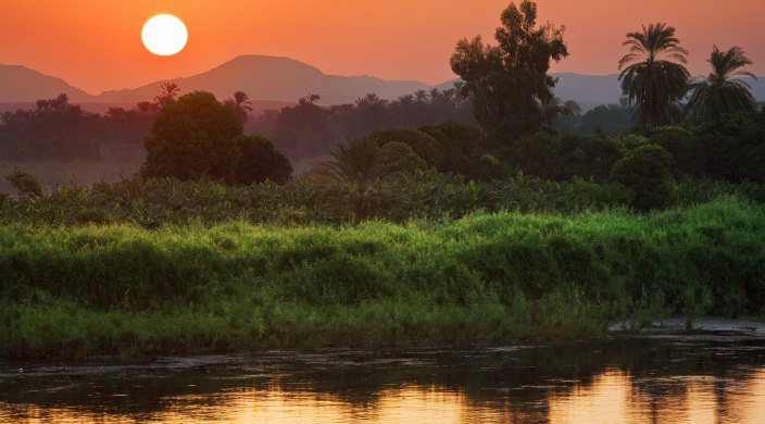 Bank of the Nile River beneath a shining red sunset