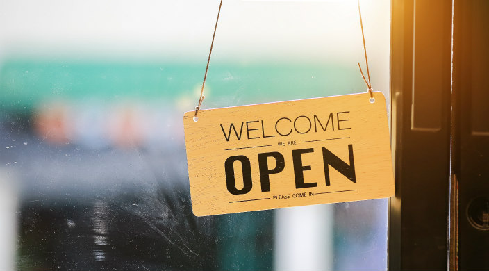 Sign hanging in a window reading Welcome We Are Open