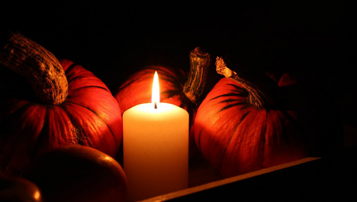 Prayer candle in the dark surrounded by pumpkins and gourds