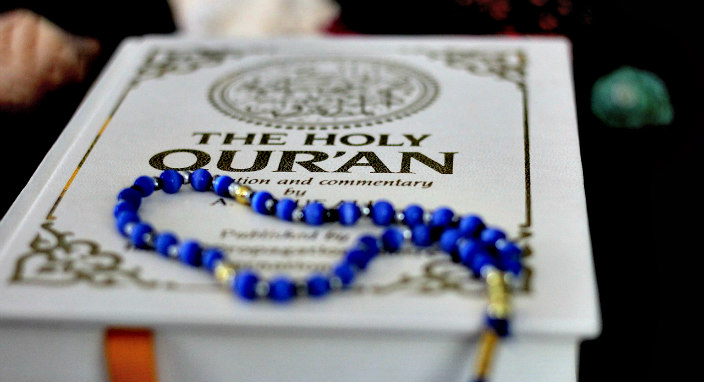 Closeup of an ornate white and gold Quran with blue prayer beads lying on top 