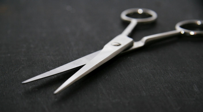 Silver scissors laying open on a black surface in the shadows 