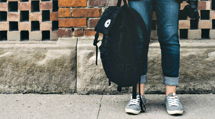 Teen wearing Converse and holding backpack against a brick wall