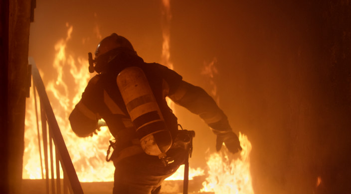 Firefighter from behind climbing steps to a building in a raging fire