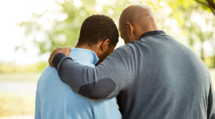 Back view of an older man with his arm around a younger man as if consoling him
