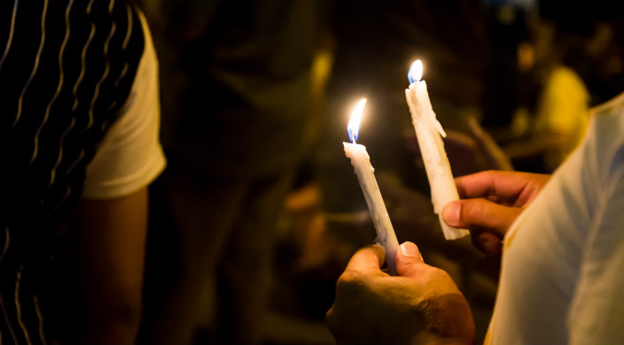 Hand holding two candles in the darkness as if at a candlelight vigil