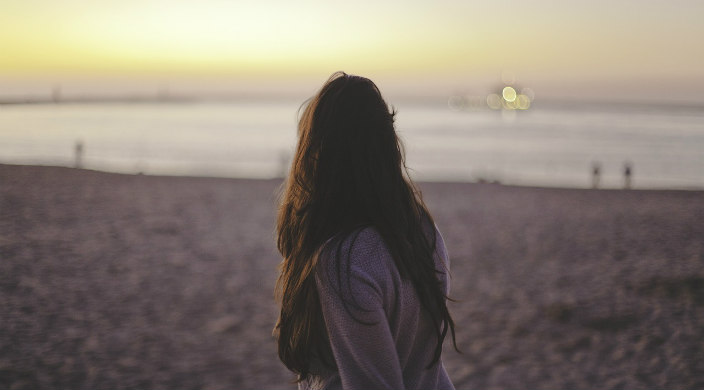 Woman in a sweater standing on a beach with her back to the camera 