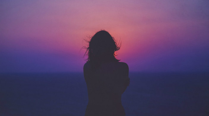 Silhouette of a woman staring into a pink sunset 
