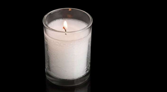 White Yahrzeit candle burning against a black background 
