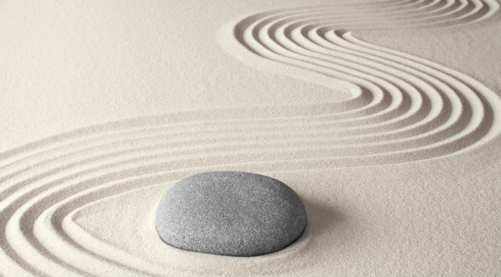 A smooth grey rock in sand surrounded by a swirl pattern in the sand 