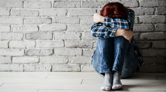 woman sitting on floor with arms around her knees and her head down