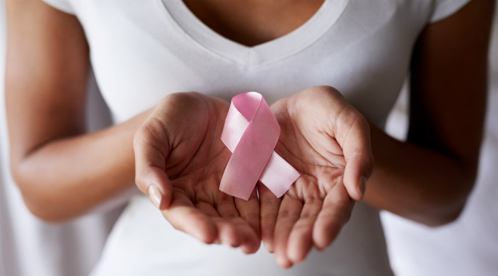 Woman of color with palms open holding a pink ribbon representing breast cancer awareness