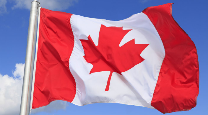 Canadian flag on flagpole with bright blue sky in the background