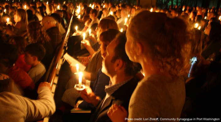 Group of people holding candles in a darkened room as if at a service 