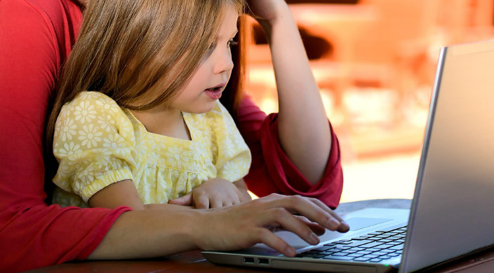 Young child sitting on an adults lap while looking at a laptop screen as if watching videos together