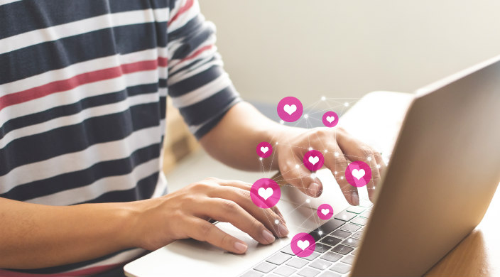 Closeup of a mans hands over a laptop keyboard with heart icons above it as if to signify online connection