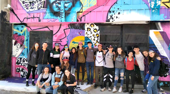 Group of high schoolers standing in front of a large colorful mural