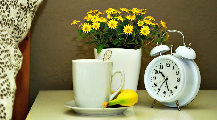 Bedside table with an alarm clock flowers and a mug of tea