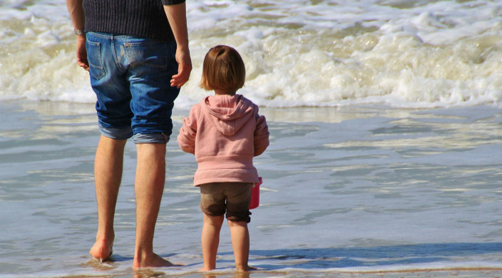 Father and young childen facing the ocean with their feet in the water