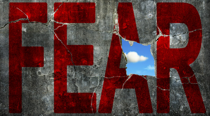 Fear written in red on a wall with a small hole of blue sky and white cloud behind