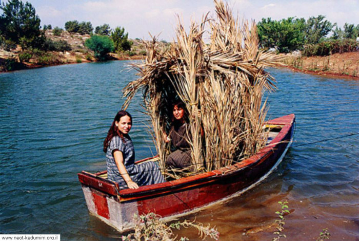 Two women in a canoe with a sukkah built upon it 