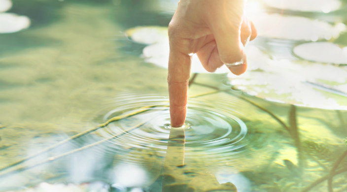 Right hand index finger making concentric circles in a light-filled pond