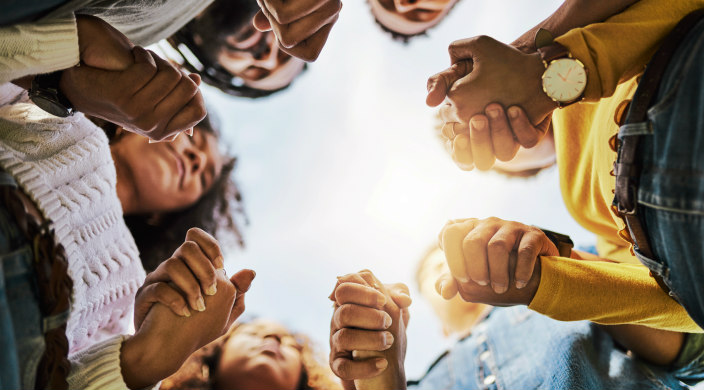 Shot from the ground up of a group of Black men and women holding hands as if in friendship or support 