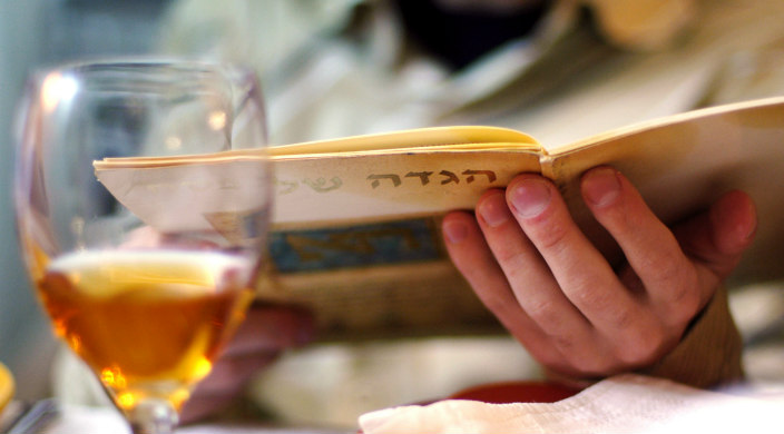 Closeup of hands holding a Haggadah with a glass of white wine in view