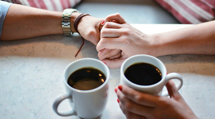Two people holding hands over mugs of coffee