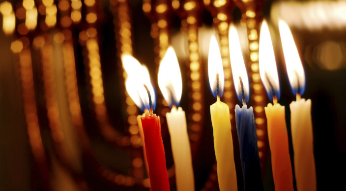Lit Hanukkah candles in the foreground; out of focus hanukkiyah in the background