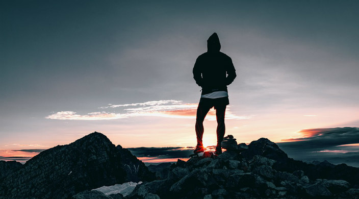 Hiker standing at the top of a mountain facing a sunset