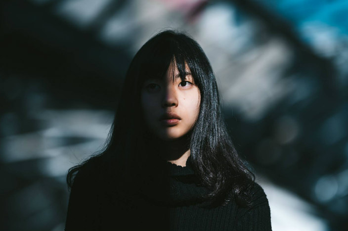 Young woman with dark hair and bangs standing partially in shadows