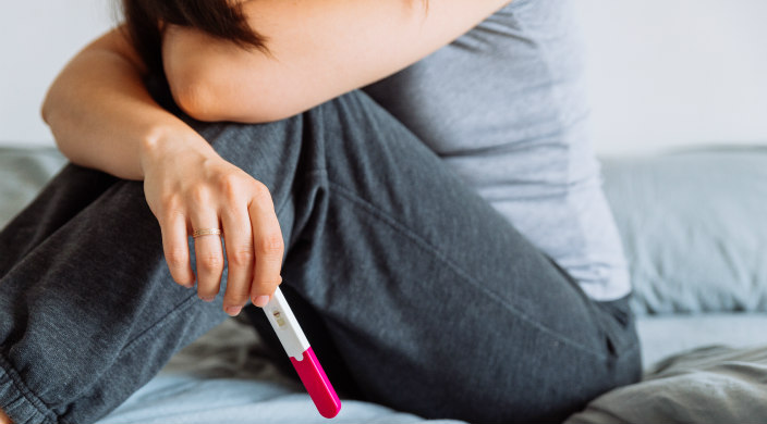 Woman sitting on bed with negative pregnancy test stick in her hand