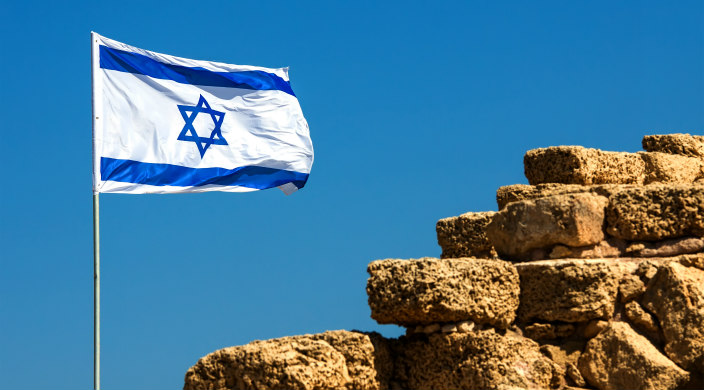 Israeli flag against blue sky, next to rocks