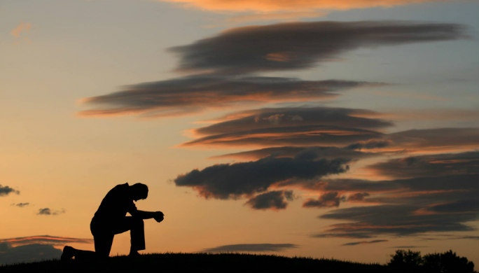 Silhouette of a man kneeling against a sunset