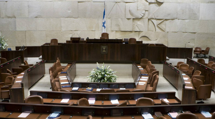 Empty chamber of the Knesset with Israeli flag at the front of the room