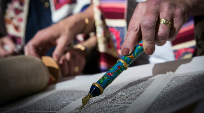 Woman's hand holding yad and pointing to Torah text